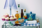 Desserts on cake stand in front of table lamp with blue lampshade and various kitchen utensils