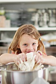A little girl kneading dough in a mixing bowl