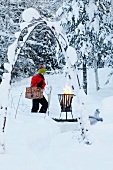 Woman carrying picnic hamper towards fire basket in snowy garden
