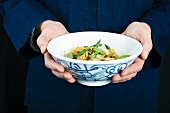 Person hält Schale mit würzigem Fischsalat (Asien)