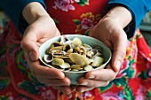A person holding a bowl of Venus clams with limes and chilli paste