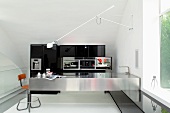 Schwenkarm einer Wandleuchte über Küchentheke aus Edelstahl und Retro Barhocker in minimalistischer Küche mit schwarzem Einbauschrank
