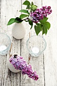 Violetter Flieder in Vasen und Teelichter auf Holztisch