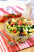 A bowl of pasta salad with green beans, peas, tomatoes, olives and spring onions