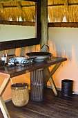 Rustikaler Waschtisch mit Schüssel und Spiegel in afrikanischer Hütte mit Strohdach