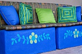 Sitzpolster und bunte Kissen in grünem und blauem Ton auf blauen Kuben mit Blumenmuster