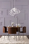 Moderne Hängelampe über rundem Esstisch mit Stühlen aus Holz und Metallgestell vor dreidimensional gestalteter Wand
