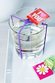 Chocolates with greetings and pictures on wrappers and glass of water with purple rubber band