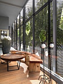 Loggia mit rustikal eleganten Holzmöbeln vor Glasfassade und Schiebeelementen aus Metallgitter