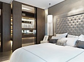 Doppelbett mit gepolstertem Kopfteil neben Ankleide mit offenen Schiebetüren im modernen Schlafzimmer
