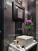 Marble basin on washstand against wall with mosaic tiles in iridescent shades of purple