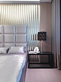 Corner of bedroom - bedclothes and upholstered headboard of double bed in matching, shimmering fabric