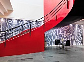 Curved staircase with red stringer walls against artistic wall in spacious foyer