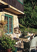 Sonnenterrasse eines Natursteinhauses; gemütich gestaltet mit Vintagemöbeln und Blumentöpfen