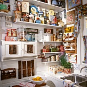 Shelving on kitchen wall holding large collection of tin cans and curiosities: small kitchen cupboard decorated with old wooden moulds