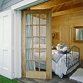 Freundliches Schlafzimmer in einem Holzhaus mit Fenstertür, Dachbalken und einem Doppelbett aus Metall