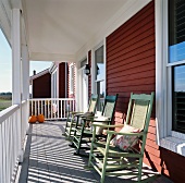 Row of rocking chairs on sunny, roofed veranda of wooden house