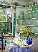 An extensive collection of Fire King crockery in pastel green in the corner of kitchen with a sash window and a round table