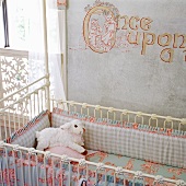 Antikes, weisses Kinderbettchen, mit Bettwäsche in Pastelltönen steht an einer beschrifteten und bemalten Wand