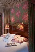 Canopied bed with heavy curtains, wallpaper, bedside lamps and pillows in floral patterns