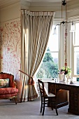 Antique desk in bay window with gathered curtains in traditional setting