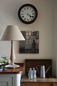 Simple table lamp on kitchen base unit and antique clock on wall above old wooden table