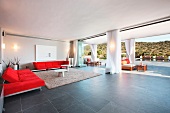 Designer Wohnraum mit roter Polstergarnitur vor offenen Terrassenschiebetüren