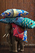 Elefant Figur aus Holz mit buntem Kissenstapel auf Rücken vor Bambusvorhang