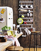 Metal rack of hooks for crockery, stool, table and fridge in rustic kitchen with wooden wall