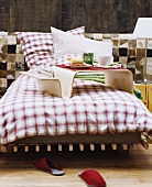 Bed with gingham flannel bed linen against wall clad in animal-skin patchwork and wood