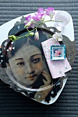 Place setting with delicate orchid spray in beaker on white china plate and metal plate with portrait of Japanese woman