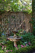 Verwitterter Steinbrunnen vor Holzzaun im Garten