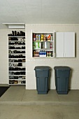 Grey plastic bins below open wall-mounted cupboard and shoe rack in utility room