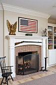 Fireplace with white-painted mantelpiece below American flag on wall of country house interior
