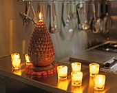 Glass tea light holders with lit candles next to cone-shaped candle on kitchen surface