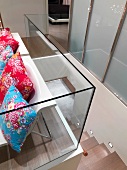 Treppenabgang mit Glasbrüstung und bunten Zierkissen mit floralem Muster auf zwei Designerstühlen