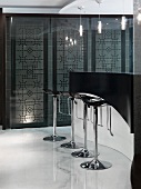 Moderne Küchentheke in Schwarz mit verchromten Barstühlen auf weißem Marmorboden