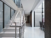 Weisser Treppenaufgang mit Metallhandlauf im offenen Wohnraum; an der Seite die Esszimmerstühle