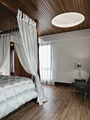 Modernes Schlafzimmer mit Holzboden und Holzdecke; ein rundes Deckenfenster sorgt für mehr Helligkeit im Raum