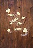 Letters made from biscuits, spelling out 'The Game of Love', with heart-shaped biscuits and sugar