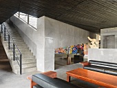 Minimalistische Halle mit Treppe in Betonausführung und Couchgarnitur vor Tisch aus Mahagoniholz
