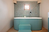 Blaugraue Treppenstufen an freistehender Badewanne vor Wand mit Mosaikfliesen im Retrostil