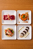 Various appetisers on four square plates