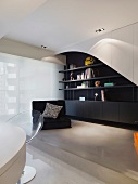 Moderner Wohnraum - schwarzer Bodensessel vor schwarz weißem Einbauregal auf Podest
