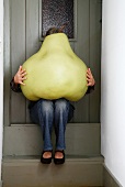 Woman sitting on front door step with huge model pear on lap