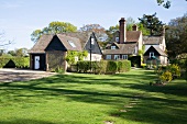 Altes, englisches Anwesen mit grosser Rasenfläche und Hecken vor verschiedenen Gebäudeteilen in sommerlicher Stimmung