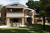 Interlocking cubes of a two-storey, flat-roofed housing complex with exposed brickwork; table and chairs on sunny terrace