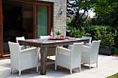 White wicker armchairs around large wooden table in front of open terrace doors in garden