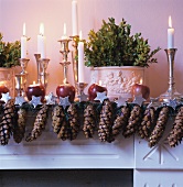 Mantelpiece festively decorated with fir cones and lit candles in candlesticks