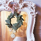 Christmas decorations and wreath of leaves hanging on mirror with ornate, white wooden frame